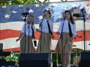 Three women singing in front of an American Flag