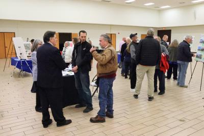 Image of people attending an open house.  Having conversations in small groups, and interacing with exhibits.  